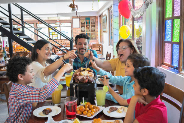 feliz familia almorzando '' fritanga '' una comida típica colombiana - latin family fotografías e imágenes de stock