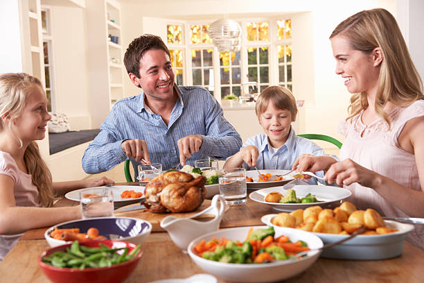 happy family having roast chicken dinner at table - gebraden vlees stockfoto's en -beelden