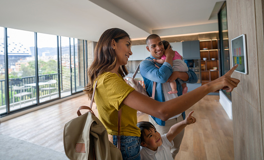 Happy Latin American family leaving the house locking the door using automated security system - smart home concepts. **DESIGN ON SCREEN BELONGS TO US**