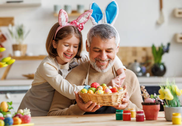 Happy family loving grandfather and cute little girl granddaughter embracing while painting Easter eggs stock photo