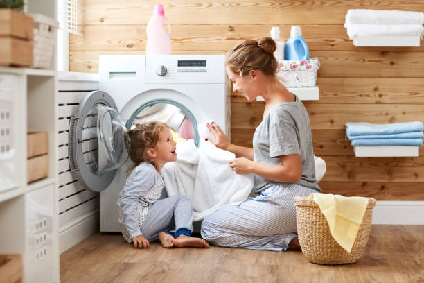 gelukkige familie moeder huisvrouw en kind in wasserij met wasmachine - wassen stockfoto's en -beelden