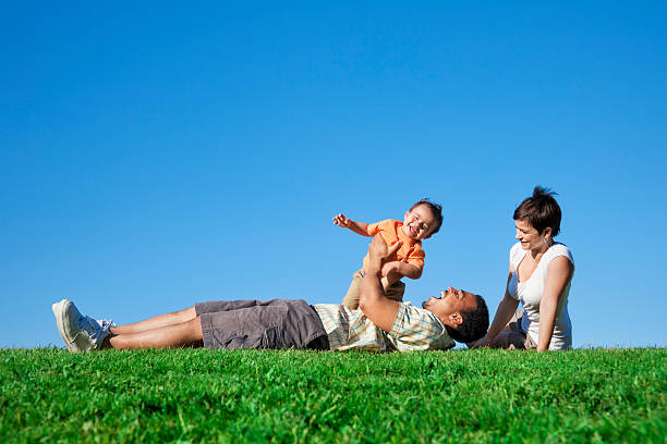 Happy Family Playing in The Park Photo of a young family enjoying a day in the park on a sunny summer day. tickling beautiful women pictures stock pictures, royalty-free photos & images