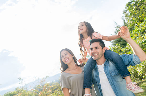 Happy family portrait at the park Happy family portrait at the park carrying daughter on shoulders and looking away at the landscape colombian ethnicity stock pictures, royalty-free photos & images