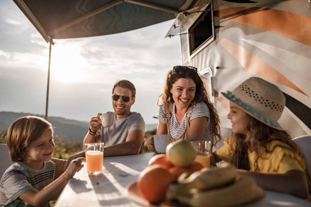 Happy family talking at picnic table by the camper trailer in nature. stock photo