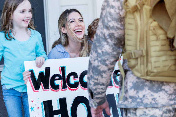 Happy family welcomes home Army dad Excited family welcomes home their military husband and dad. The man's wife is holding a 'Welcome Home' sign. soldiers returning home stock pictures, royalty-free photos & images