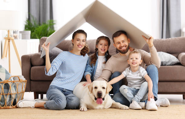 Happy family with dog enjoying new home Young family with kids and dog holding roof over heads and smiling happily while sitting in living room of new apartment moving house photos stock pictures, royalty-free photos & images