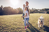 Beautiful happy family is having fun with golden retriever outdoors. Mother, father and daughter are running with dog labrador in park.