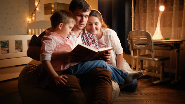 Happy family with little boy reading book at night before going to sleep. Concept of child education and family having time together at night. stock photo