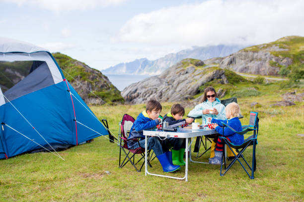 Happy family with three kids, wild camping in Norway summertime, people having breakfast adn coffee on a cliff next to a fjord stock photo