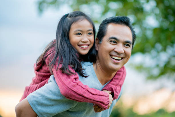Happy father and daughter in the summertime A 8 year old girl holds onto her father's back and they smile genuinely as they look into the distance. philippines girl stock pictures, royalty-free photos & images