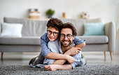 istock Happy father and son having fun at home. Dad lying on carpet carrying boy on back and smiling together to camera 1312598143