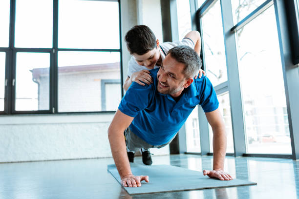 pai feliz fazendo push up exercício com filho na parte de trás na academia com espaço de cópia - son dad workout - fotografias e filmes do acervo