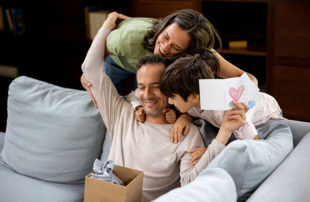 Happy father opening his gift for Father's Day Happy father opening the gift from his family for Father's Day and reading the card - lifestyle concepts fathers day stock pictures, royalty-free photos & images
