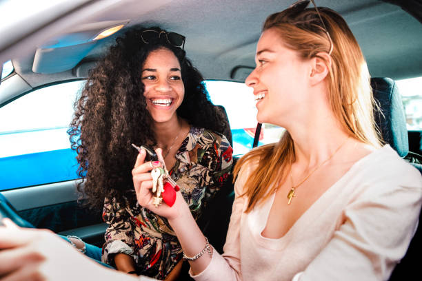 Happy female best friends having fun at car roadtrip - Transportation concept and urban ordinary life with young women girlfriends at happy travel vacation moment on the road - Bright vivid filter stock photo