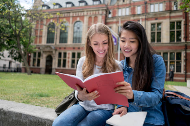 Happy female students studying outdoors Happy female students studying outdoors reading notes on a notebook - education concepts universities in uk stock pictures, royalty-free photos & images