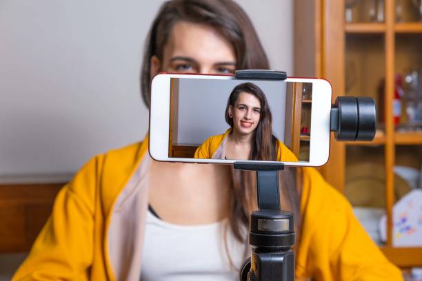 Happy female vlogger live streaming from living room using smartphone stock photo