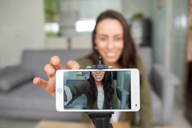 happy female vlogger recording content at home using her cell phone - smartphone filming imagens e fotografias de stock