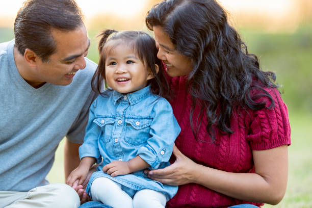 Happy Filipino family of three A little girl of two years smiles as her mom and dad  look at her and smile. She is sitting on her mothers lap and situated between her parents. filipino family stock pictures, royalty-free photos & images