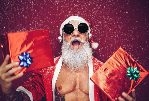 Happy Fit Santa Claus Laughing And Giving Christmas Gifts Trendy Beard Tattoo Hipster Senior Wearing Xmas Clothes And Holding Presents Celebration And