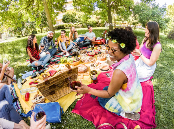 szczęśliwi przyjaciele robią piknik w publicznym parku na świeżym powietrzu - młodzi modni ludzie bawiący się, jedzący i pijąc wino - główny nacisk na afro girl face - youth, nature, friendship concept - england australia zdjęcia i obrazy z banku zdjęć
