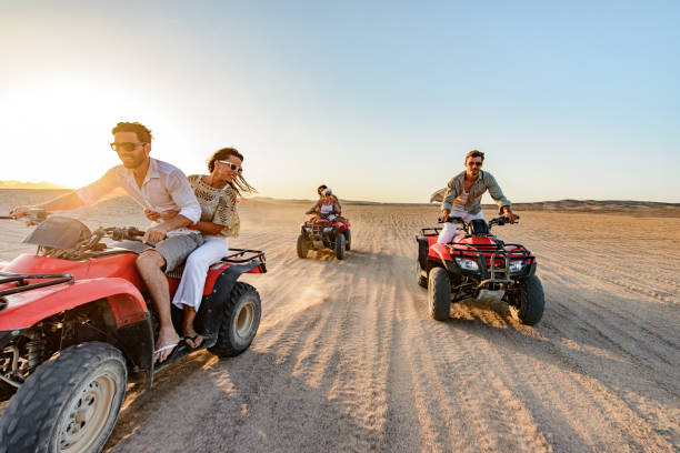 Happy friends driving quads in the desert at sunset. stock photo