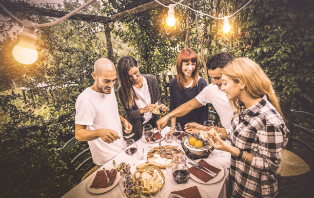 gelukkige vrienden met leuke lokale eten op tuin fest - vriendschap en vakantie concept met mensen samen bij boerderij wijngaard winery - warme vintage filter met kunstmatige elektrische verlichting - family garden,party stockfoto's en -beelden