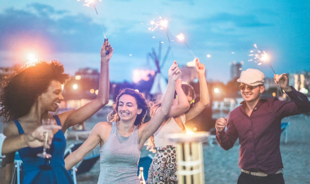 happy friends making evening beach party outdoor with fireworks - young people having fun dancing and drinking champagne - soft focus on center woman hand - vacation and nightlife concept - cargo canarias imagens e fotografias de stock