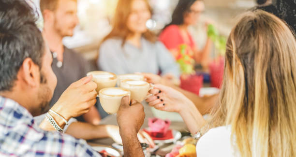 szczęśliwi przyjaciele opiekający się z cappuccino w kawiarni barowej - młodzi modni ludzie korzystający ze śniadania - przyjaźń, styl życia młodzieży i koncepcja przerwy na posiłek - skup się na dolnej ręce indyjskiego mężczyzny - england australia zdjęcia i obrazy z banku zdjęć