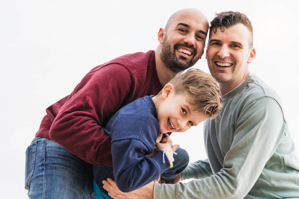 Happy gay male parents and son having fun playing outdoor in the city - Lgbt people and family love concept - Soft focus on boy face stock photo