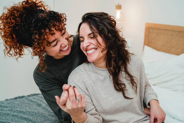 Happy gay women couple celebrating together with engagement ring in bed - Soft focus on right lesbian girl face stock photo