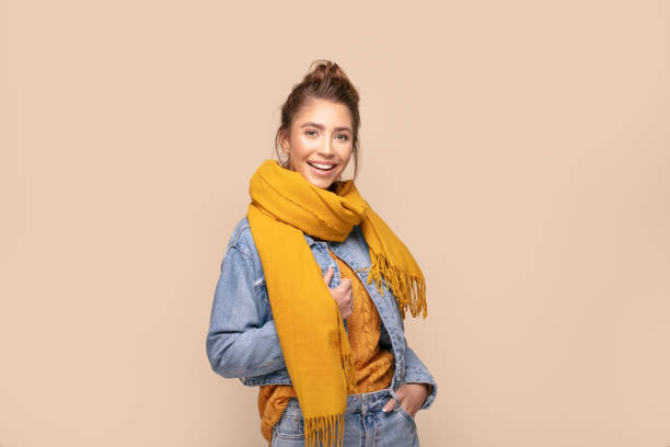 Happy girl in autumn yellow scarf. Young beautiful happy girl posing in studio wearing fashionable scarf and jeans jacket. Smiling woman looking at camera. Human emotions,, expression. Beige studio background. scarf stock pictures, royalty-free photos & images