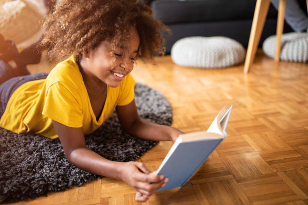 happy girl reading a book in the living room. - child reading imagens e fotografias de stock