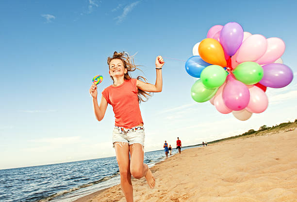 Happy girl with balloons running on the beach stock photo