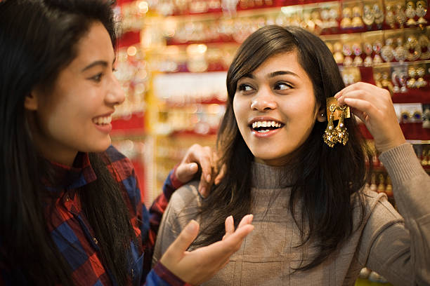 Happy girls buying earrings in jewelry shop before festival. Image of two late teen happy, Asian girls of different ethnicity selecting and buying earrings at jewelry shop just before new year and Diwali festival in India. Two people, waist up, horizontal composition and selective focus with copy space. indian jewelry stock pictures, royalty-free photos & images