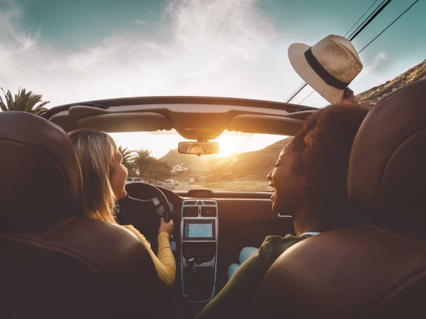 happy girls doing road trip in tropical city - travel people having fun driving in trendy convertible car discovering new places - friendship and youth girlfriends vacation lifestyle concept - happy traveling imagens e fotografias de stock