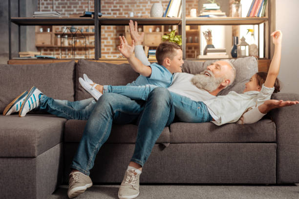 Happy grandfather playing with his grandchildren on couch Sweet moments. Happy loving grandfather bonding to his grandchildren and goofing around with them on the couch baby boomers stock pictures, royalty-free photos & images