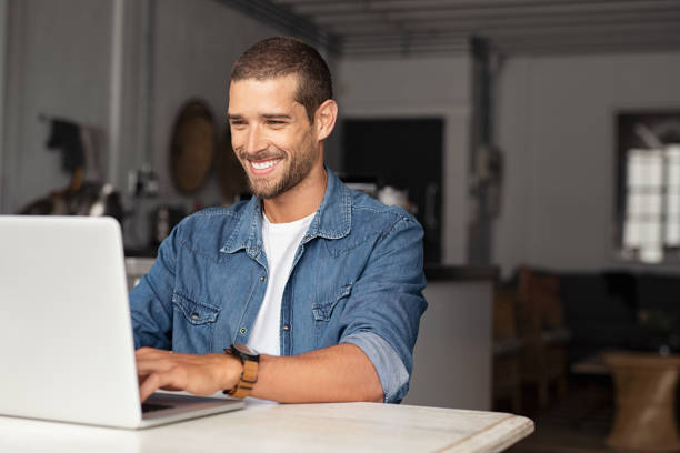 happy guy using laptop - homens jovens imagens e fotografias de stock