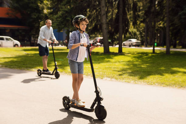 ragazzo felice con papà che guida su scooter elettrico - electric scooter foto e immagini stock