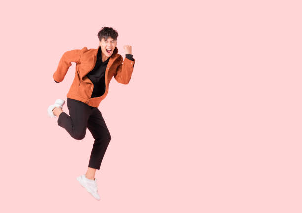 Happy handsome Asian man in fashionable clothing and jumping doing winner gesture isolated on pink background with clipping path. stock photo
