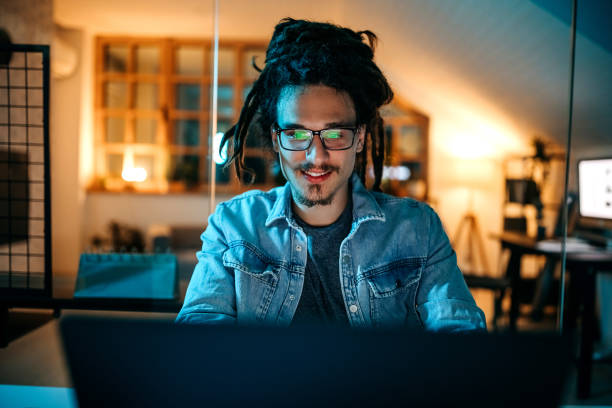 happy handsome young man using computer in his small home office - webdesigner stockfoto's en -beelden