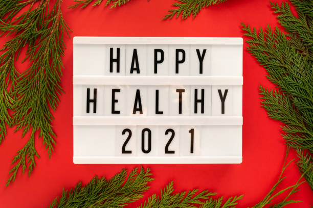 Happy Healthy 2021 year displayed on a white vintage lightbox on bright red background with juniper branches around, flat lay. stock photo