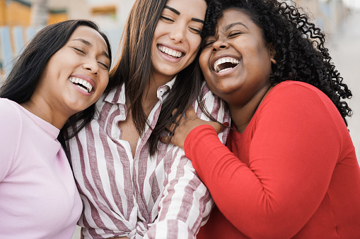 Happy hispanic women enjoy time together outdoor around city - Focus on black girl face