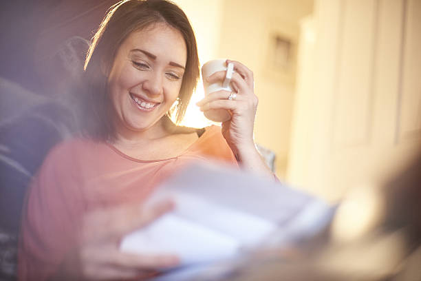 happy home finances happy young woman sat on the sofa in her living room smiling at her latest bank statement relief emotion stock pictures, royalty-free photos & images