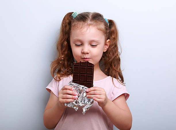 Happy kid girl eating health dark chocolate with pleasure stock photo