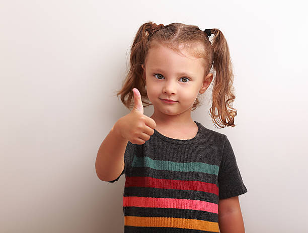 Happy kid girl showing thumb up sign and smiling stock photo