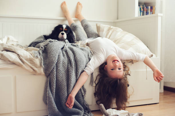 happy kid girl waking up in the morning in her bedroom with dog in bed stock photo