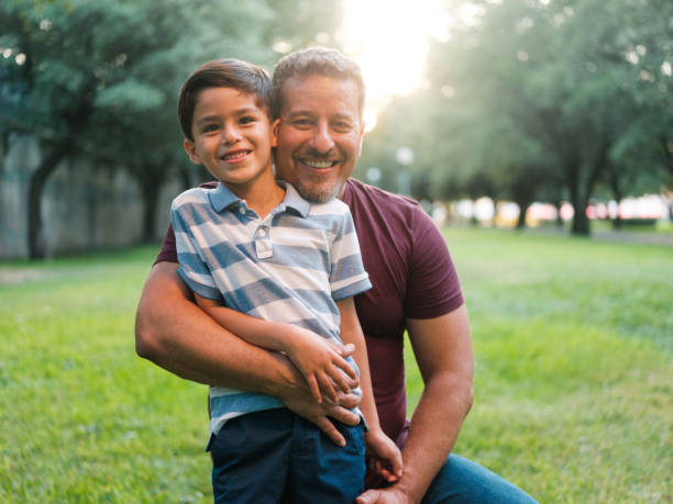 Happy latin father and little boy smiling at camera outdoors A happy latin father holding his little son outdoors, looking at the camera and smiling. medium shot stock pictures, royalty-free photos & images