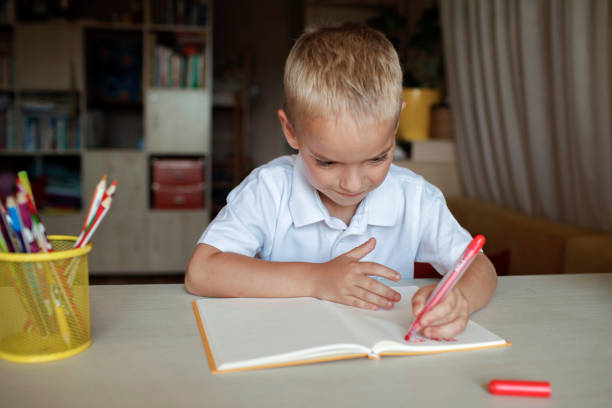 Happy left-handed boy writing in the paper book with his left hand, international left-hander day stock photo