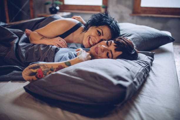 Happy lesbian couple in bed Female couple laughing while lying in the bed gay spooning stock pictures, royalty-free photos & images