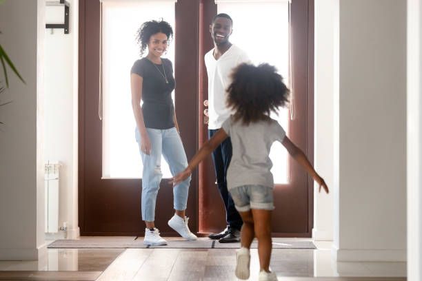 Happy little African American girl running to father, greetings Happy little African American girl running to father returning, going back home after work, greetings, daughter with attractive smiling mother in hall welcome back dad, family reunion concept returning home stock pictures, royalty-free photos & images